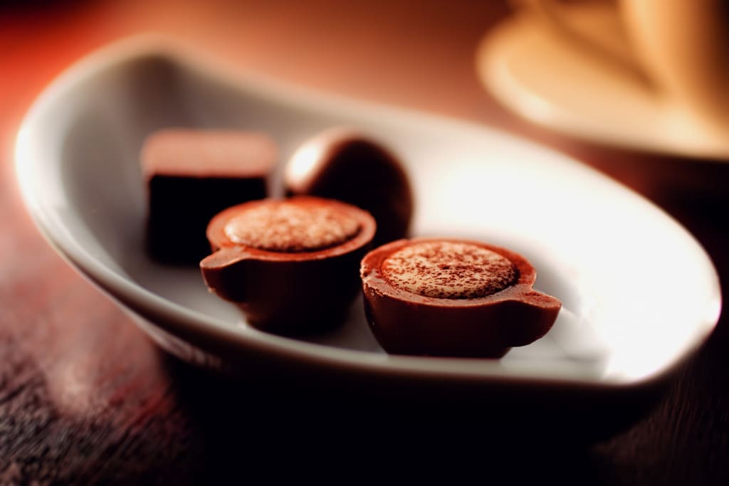 A close up of a coffee cup on a plate, with Chocolate and Praline