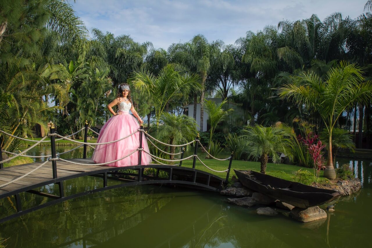 a woman in pink gown standing on a wooden bridge