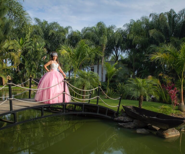 a woman in pink gown standing on a wooden bridge