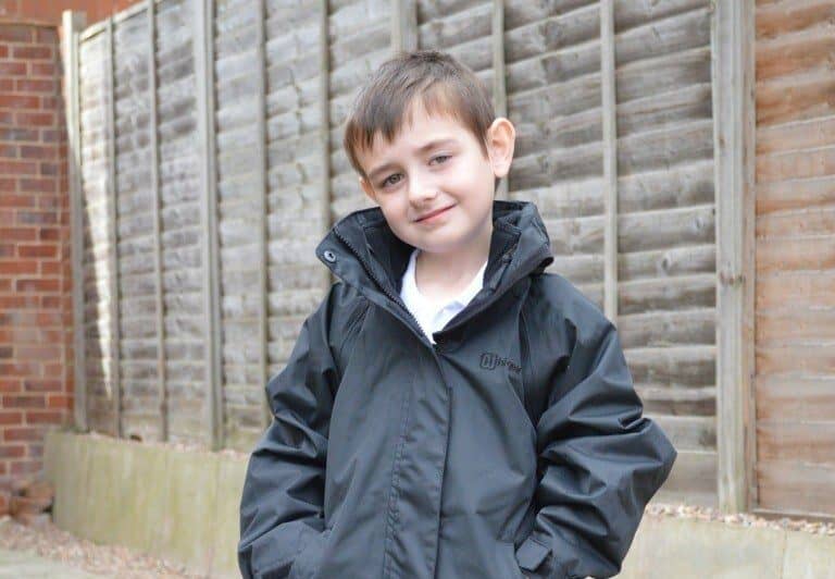 A young boy standing in front of a brick building