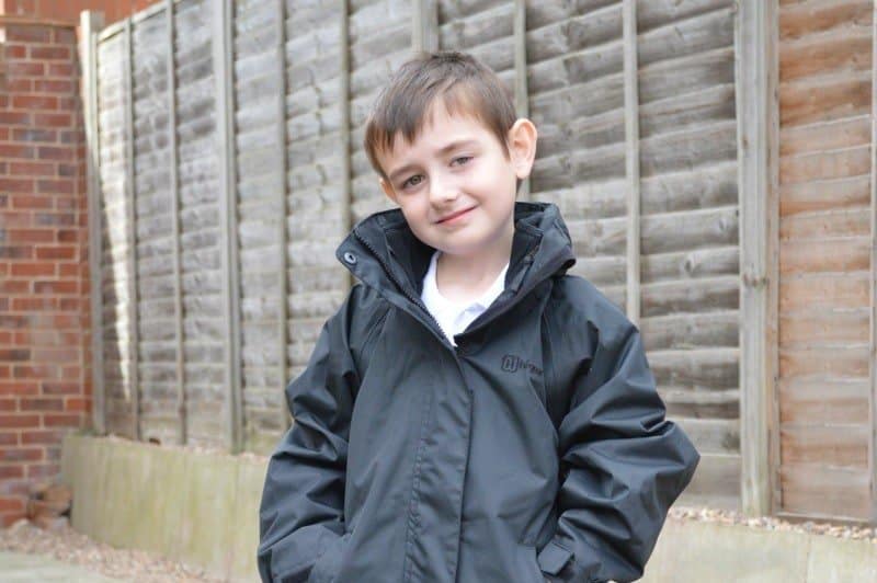 A young boy standing in front of a brick building