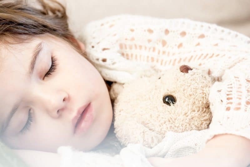 A baby lying on a bed with a teddy bear