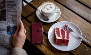 A piece of cake on a plate next to a cup of coffee