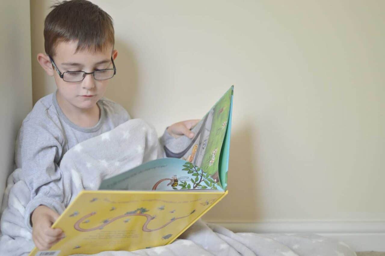 A young boy using a laptop computer sitting on top of a bed