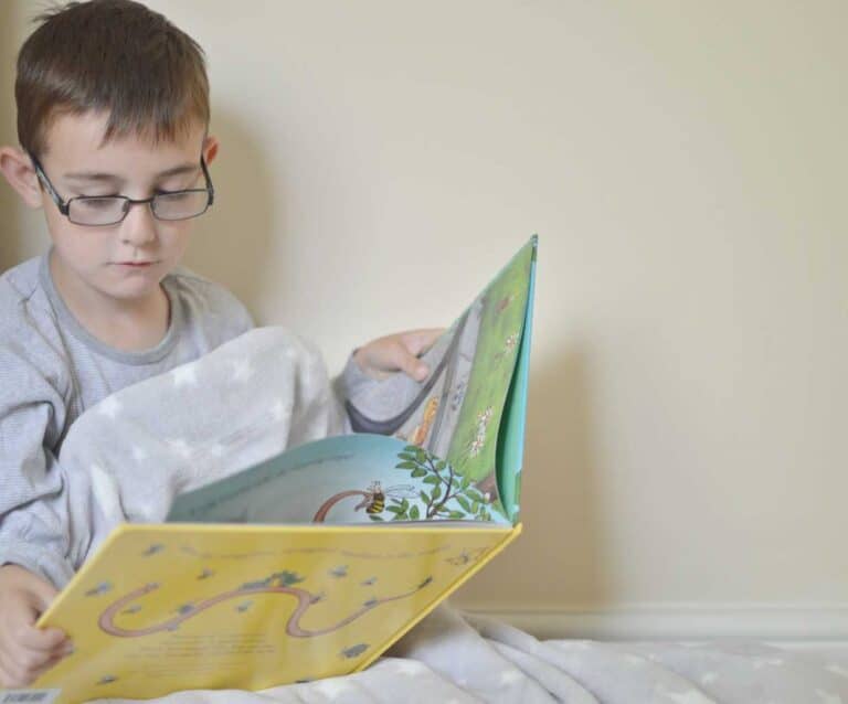 A young boy using a laptop computer sitting on top of a bed