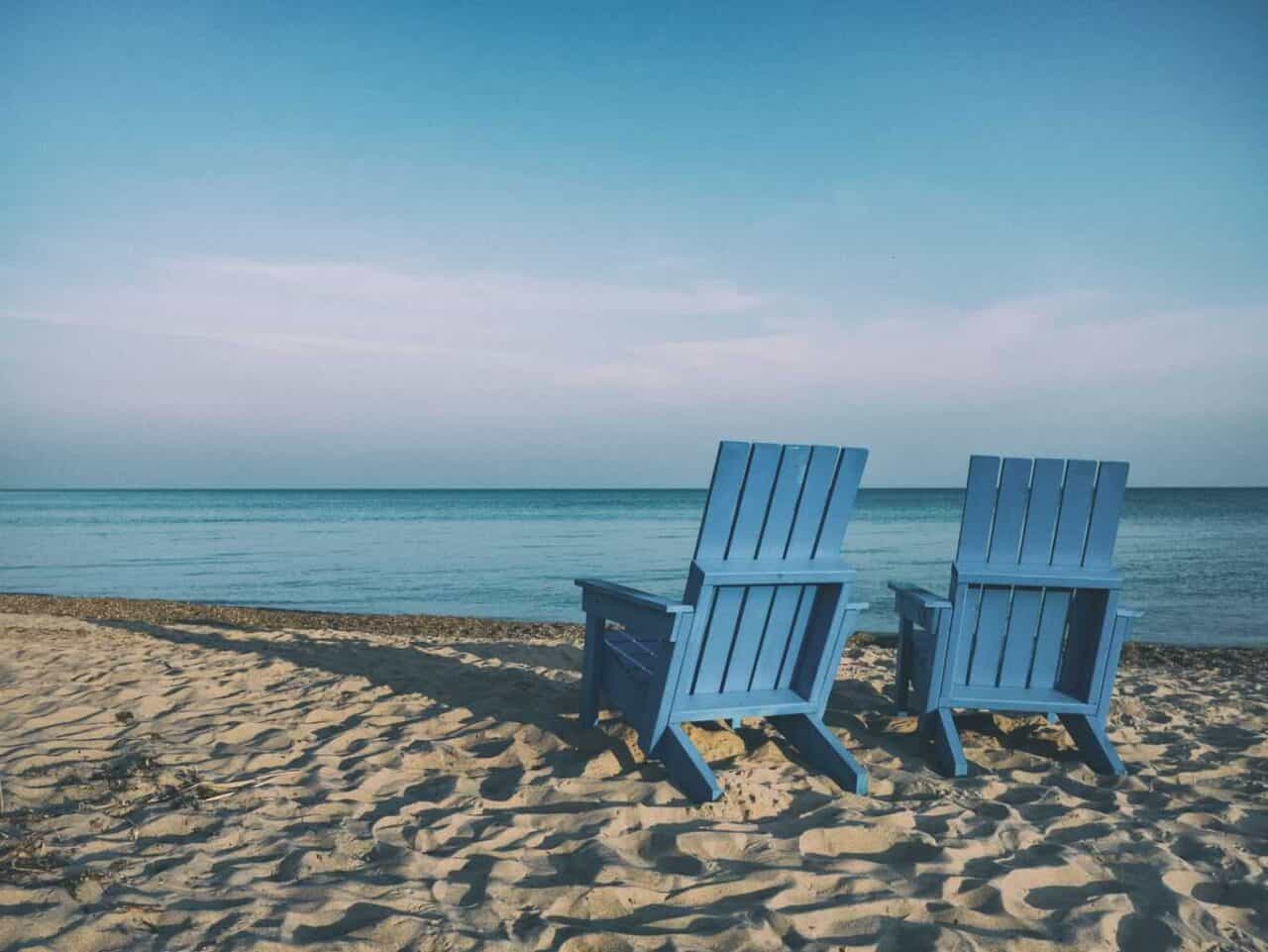 A couple of lawn chairs sitting on top of a sandy beach