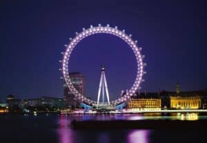 A large bridge lit up at night with London Eye in the background