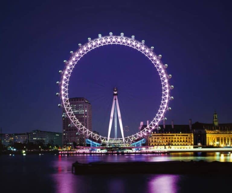 A large bridge lit up at night with London Eye in the background