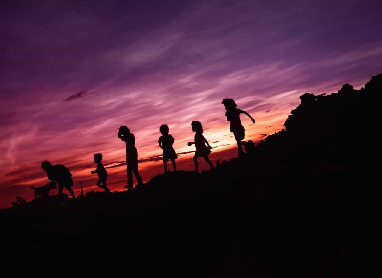 A group of people walking up a hill with a sunset in the background