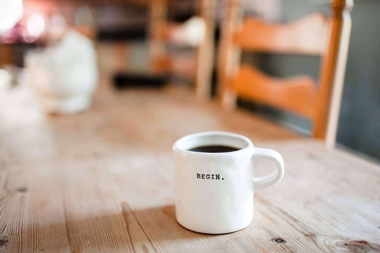 A close up of a coffee cup sitting on top of a wooden table, with Mug and Coffee bean