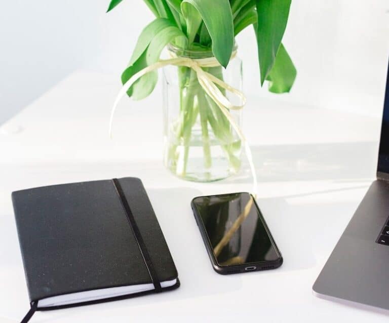 A desk with a laptop and a vase of flowers sitting on a table