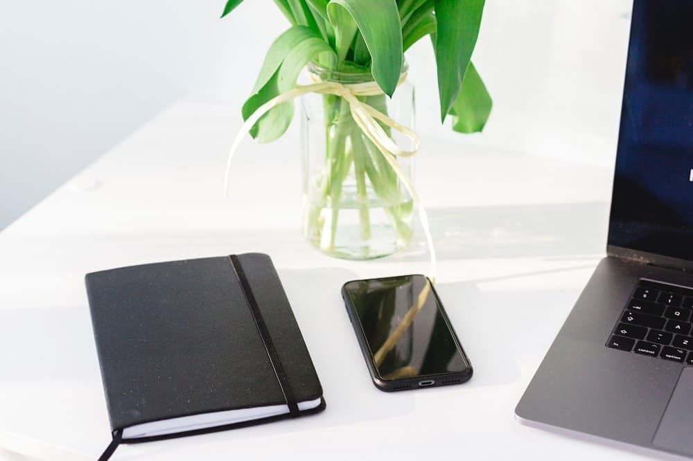 A desk with a laptop and a vase of flowers sitting on a table
