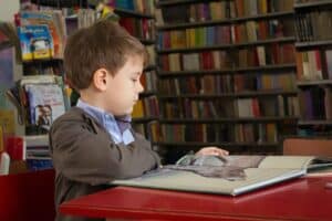 A young boy using a laptop computer sitting on top of a book shelf