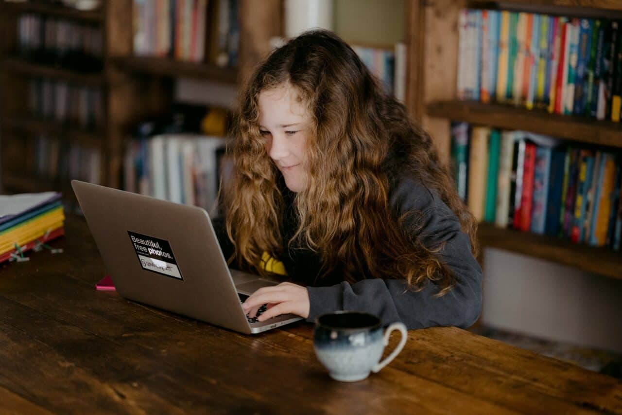 A man using a laptop computer sitting on top of a book shelf