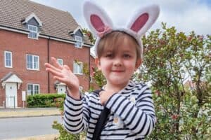 A young girl wearing bunny ears standing in front of a building