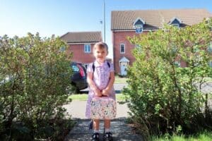 A little girl sitting on a garden path ready for school