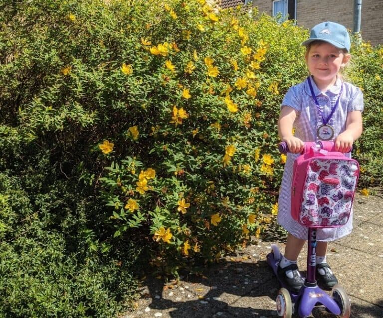 child on a purple micro scooter standing in front of a green bush