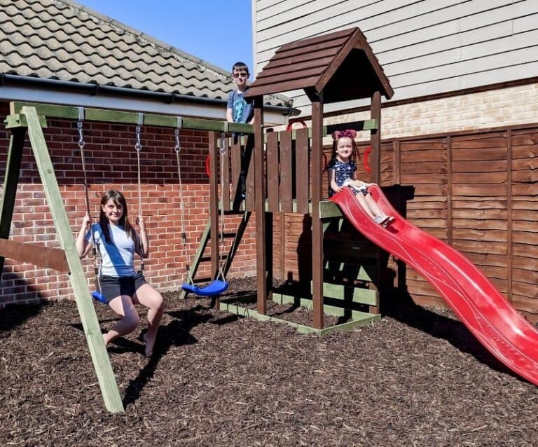 Children playing on a wooden climbing frame sitting on play bark