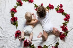 baby and toddler laying on a white blanket surrounded by flowers