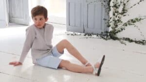 child sitting on a white wooden floor in shorts and a shirt