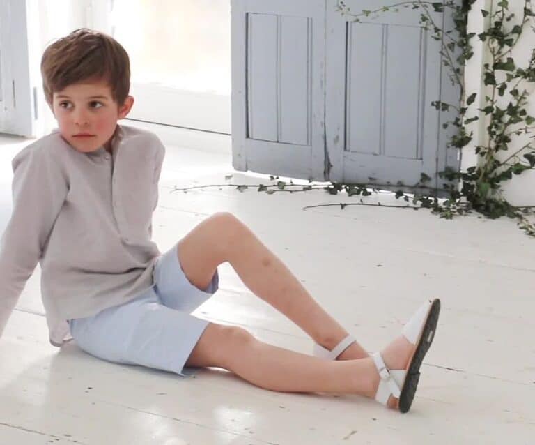 child sitting on a white wooden floor in shorts and a shirt