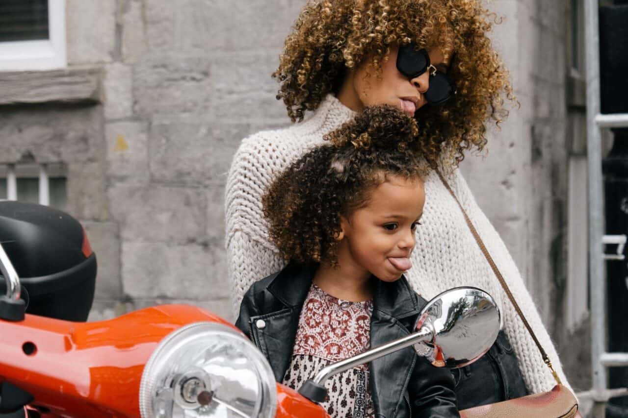 woman and girl showing their tongues besides a motorcycle mirror