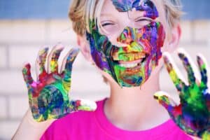 boy in pink crew neck top with paints on his hands and face