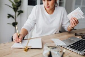 10 Healthy Money Habits - woman writing in a notepad at the desk