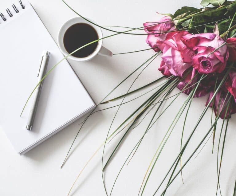 red rose flowers bouquet on white surface beside spring book with click pen and cup of cofffee