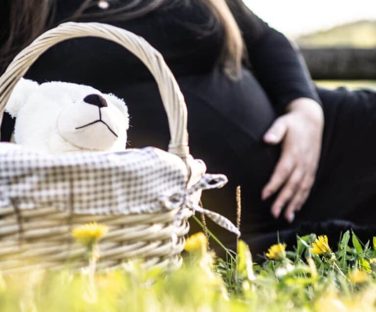 pregnant woman sitting on grass near picnic basket