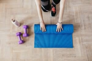 crop sportswoman unfolding sport mat on wooden floor