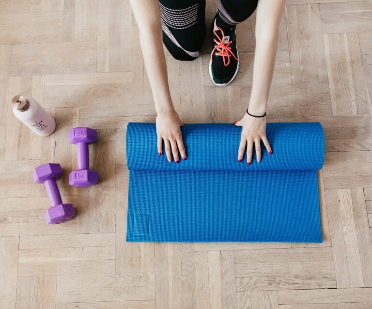 crop sportswoman unfolding sport mat on wooden floor