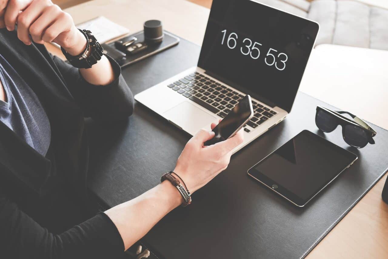 How To Take Your Business Into The Digital World - woman using a smartphone while fronting a macbook pro and black ipad