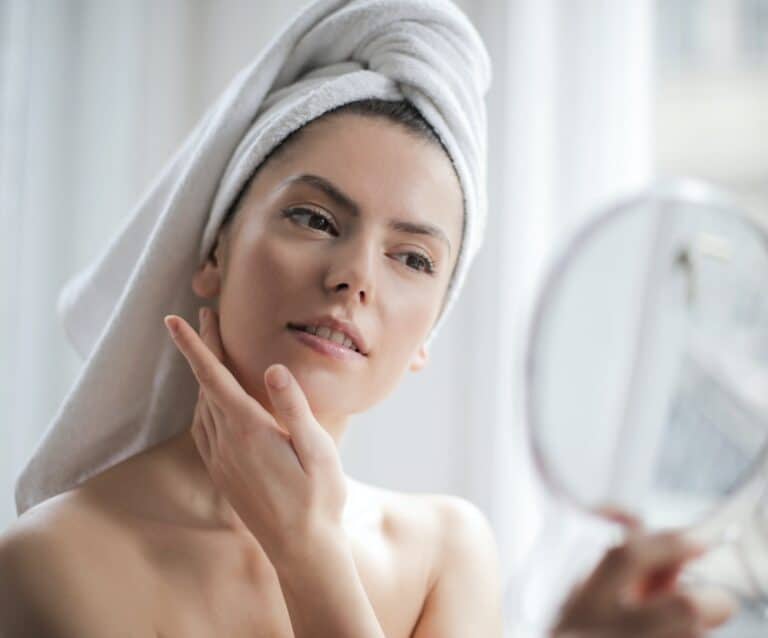 selective focus portrait photo of woman with a towel on head looking in the mirror