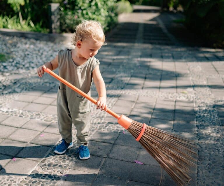 charming child sweeping concrete pavement with broomstick