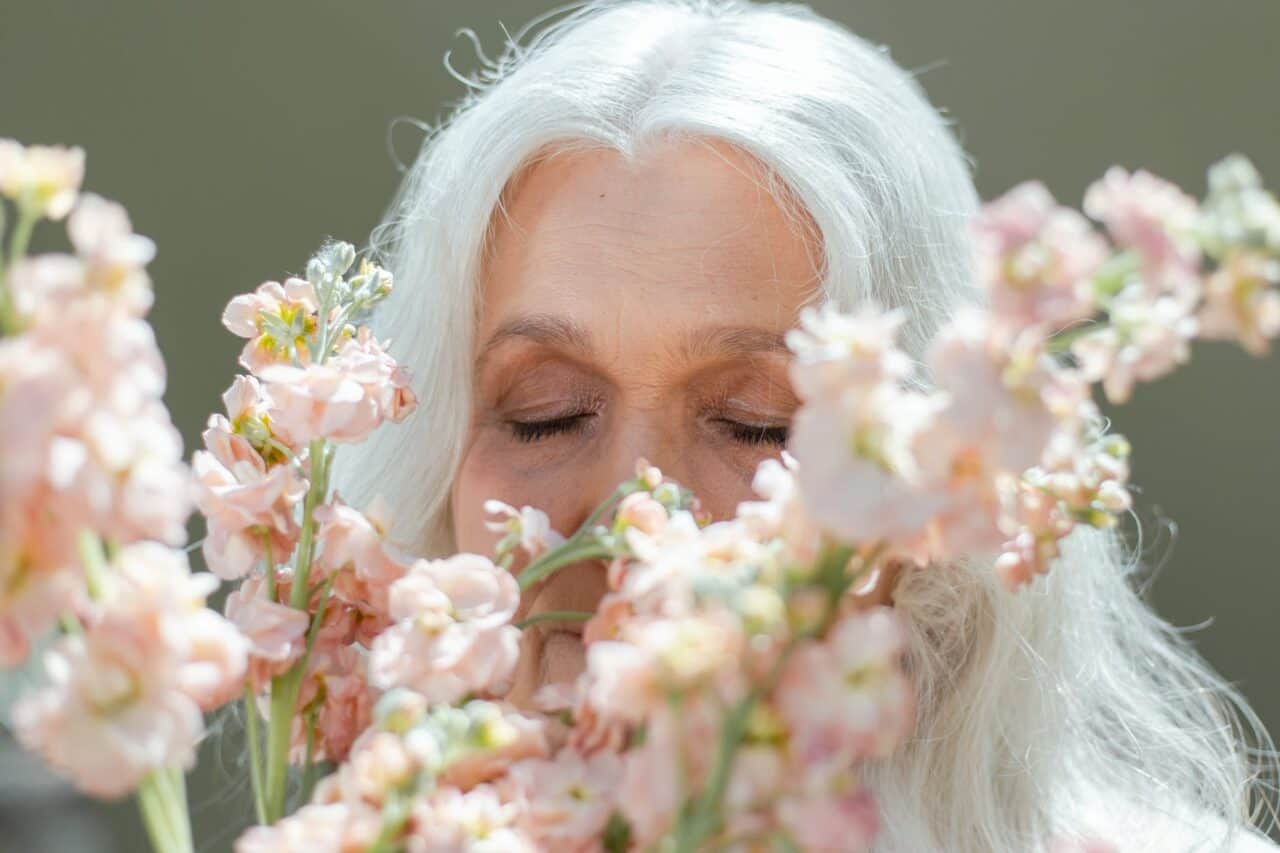 elderly woman smelling pink flowers