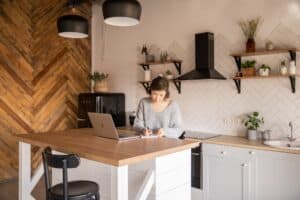 busy female freelancer with laptop taking notes in kitchen