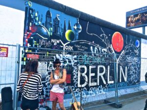 man wearing black waistcoat and white tank tops standing near a mural