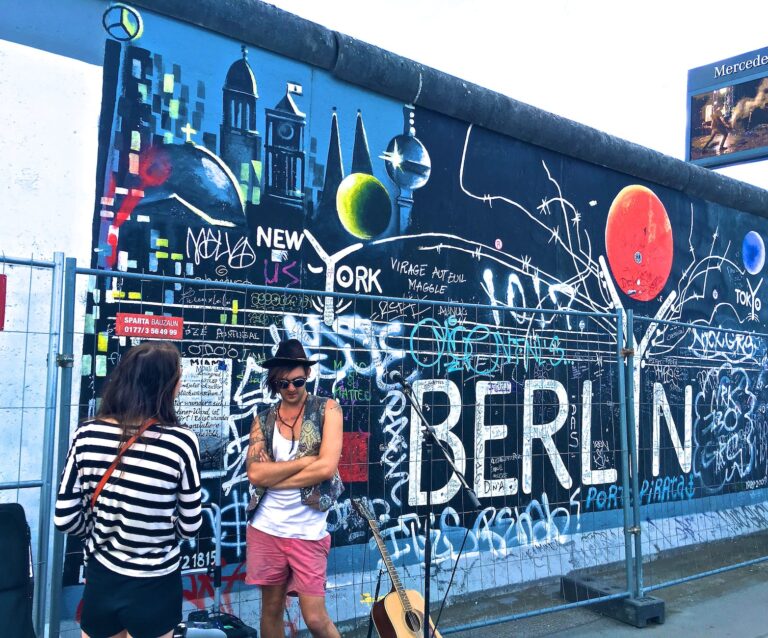 man wearing black waistcoat and white tank tops standing near a mural