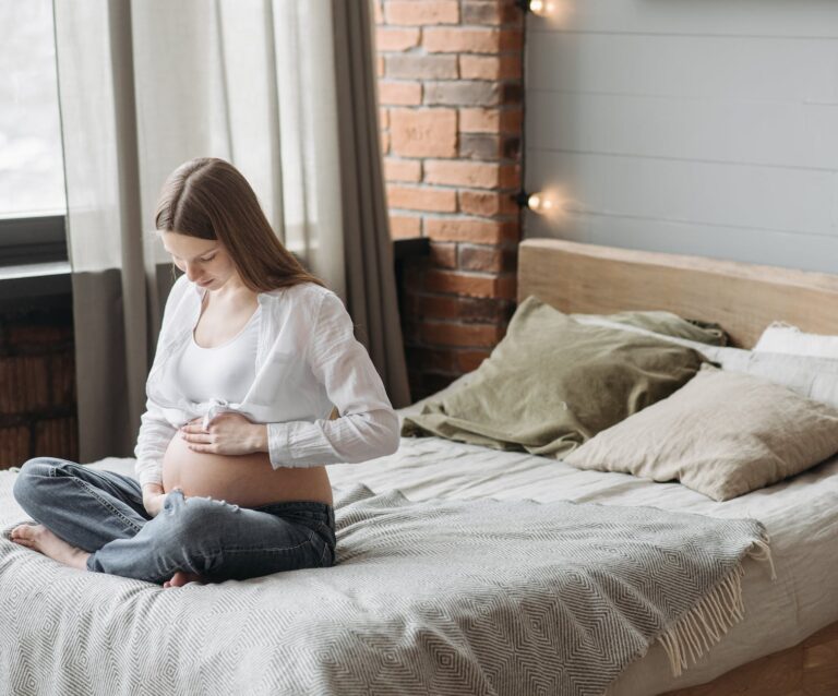 8 ways to sleep better when you're 8 months pregnant - pregnant woman sitting on bed holding her belly