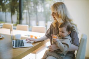 woman carrying her baby and working on a laptop